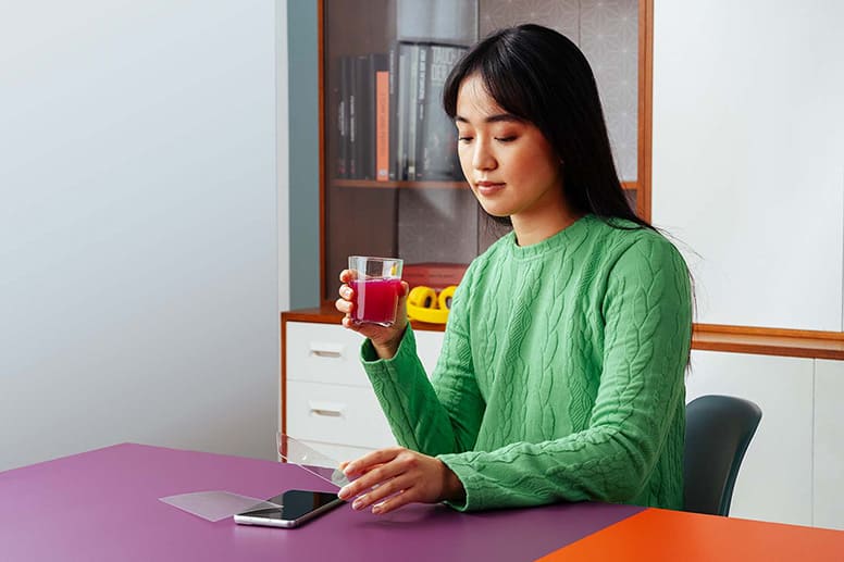 Une jeune femme avec un verre de jus dans la main utilise son téléphone et compare un verre trempé avec un film protecteur