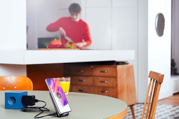Un adolescent en arrière-plan, un smartphone Samsung est posé sur une table et charge sur une station de charge à induction.