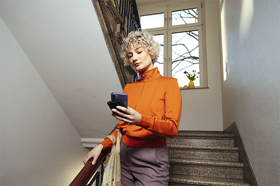Une femme descend les escaliers, son smartphone est en train d’être chargé par une batterie externe.