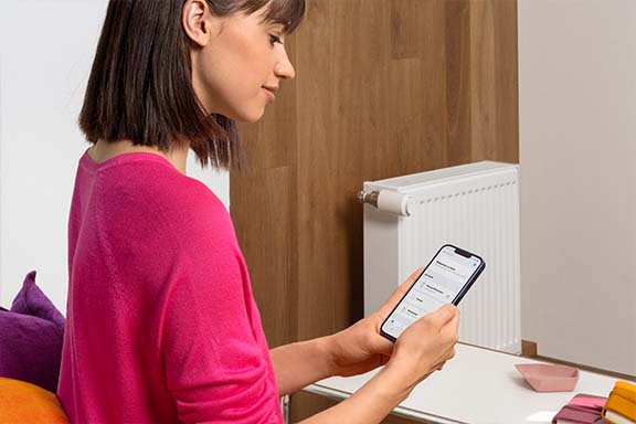 Une personne commande le thermostat via l’application.