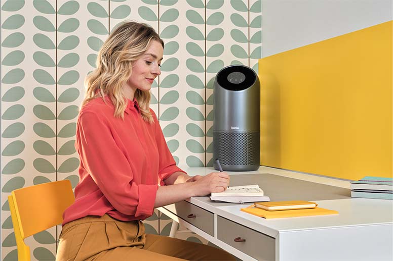 Une personne travaille à son bureau. Un ventilateur intelligent se trouve en arrière-plan.
