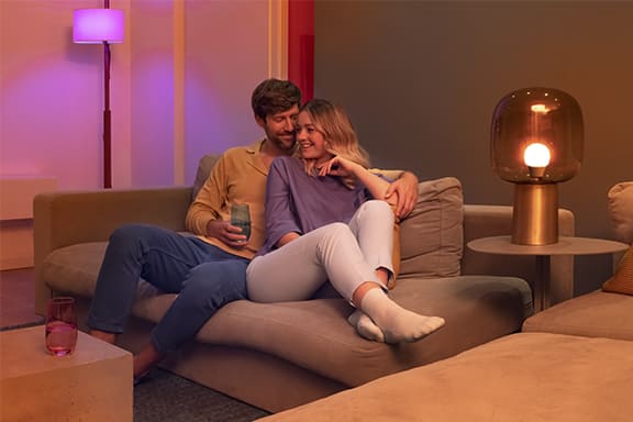 Deux personnes sont assises sur un canapé dans un salon éclairé par une lumière d’ambiance.
