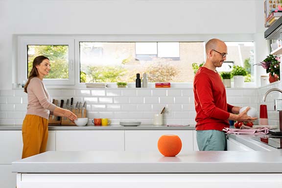 Des personnes sont dans une cuisine, au premier plan se trouve une enceinte Siri d’Apple.
