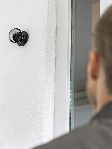 Un homme se tient devant une porte d'entrée et est filmé par la caméra de surveillance Hama